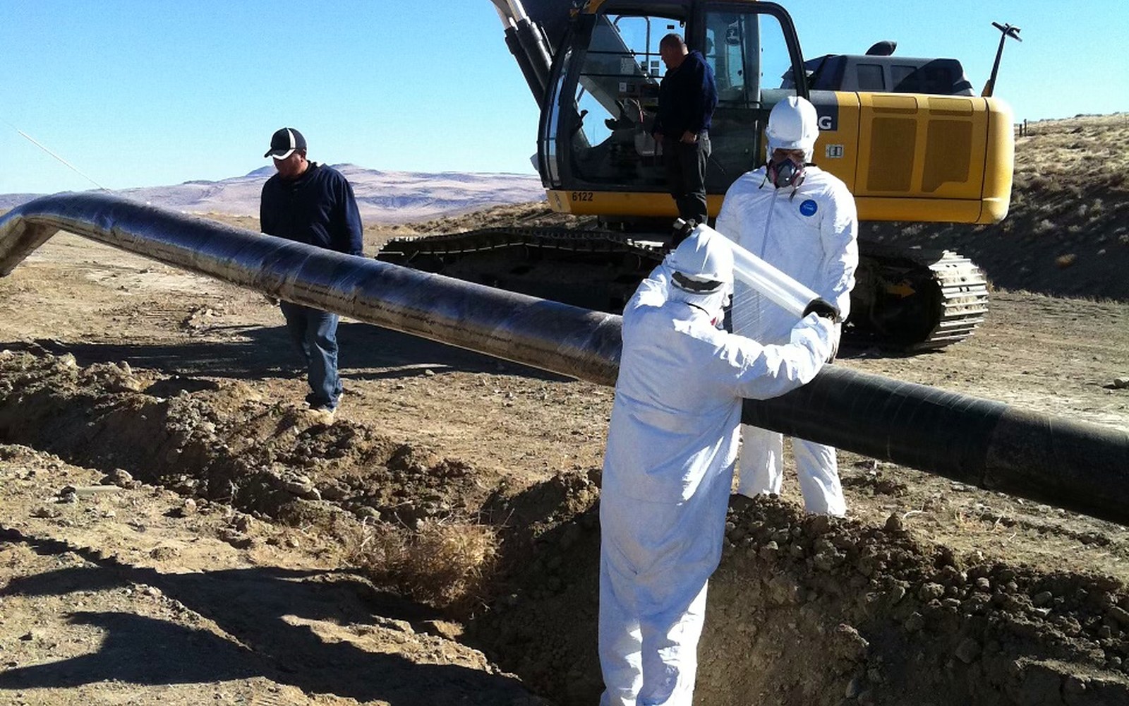 Crew in protective equipment guiding pipe clear of the ditch
