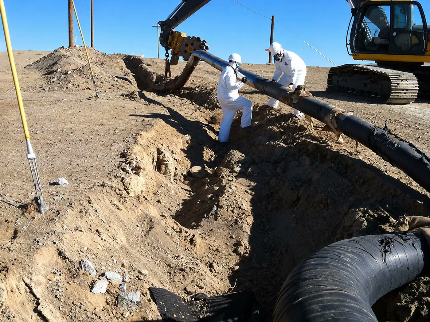 Crew in protective suits and respirators removing coated pipe from an open trench