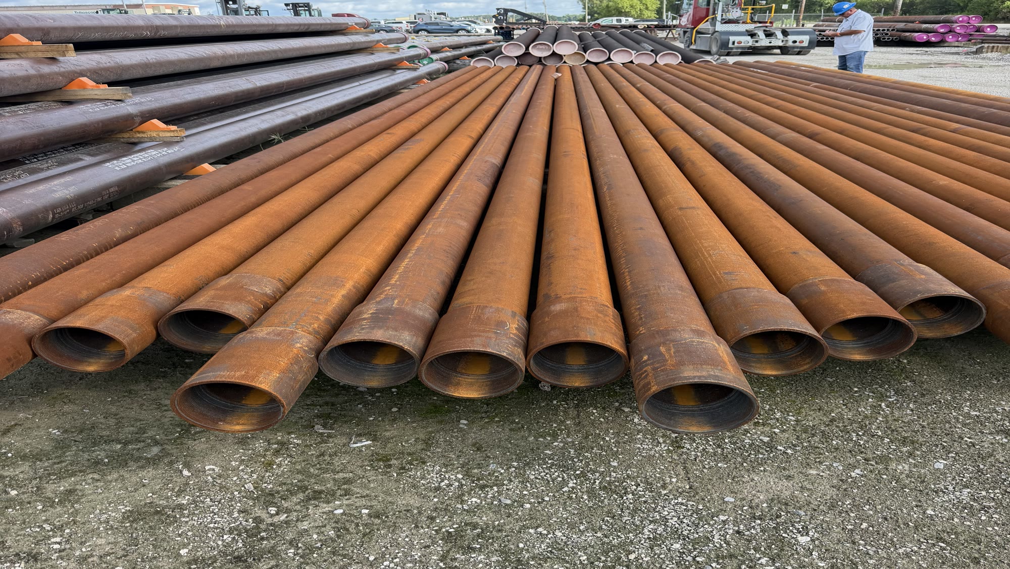 Stacked bundles of surplus steel pipe in a yard under a blue sky