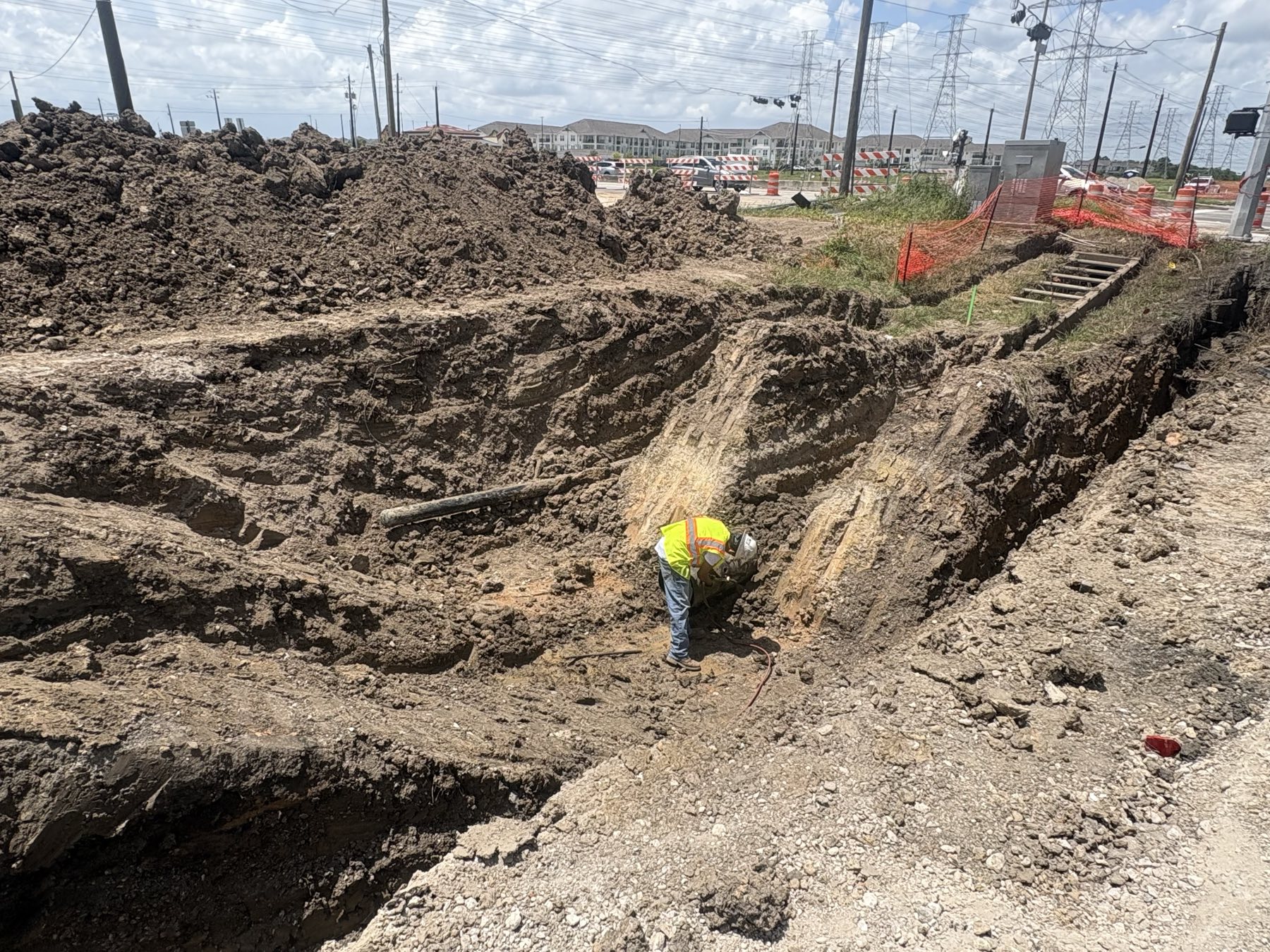 Deep excavation exposing a pipeline, with a worker working the line