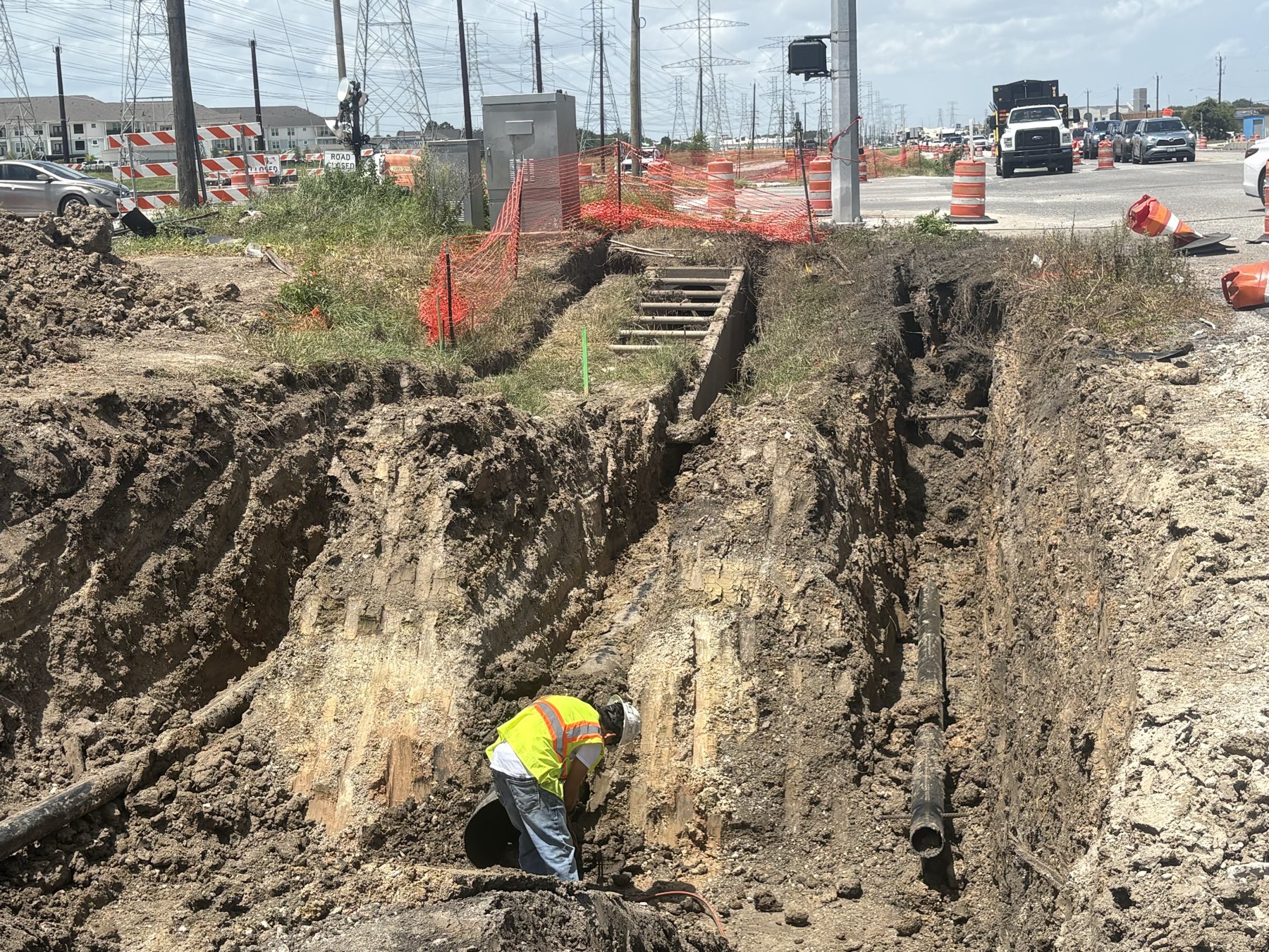 Worker exposing buried line pipe along the floor of an open trench